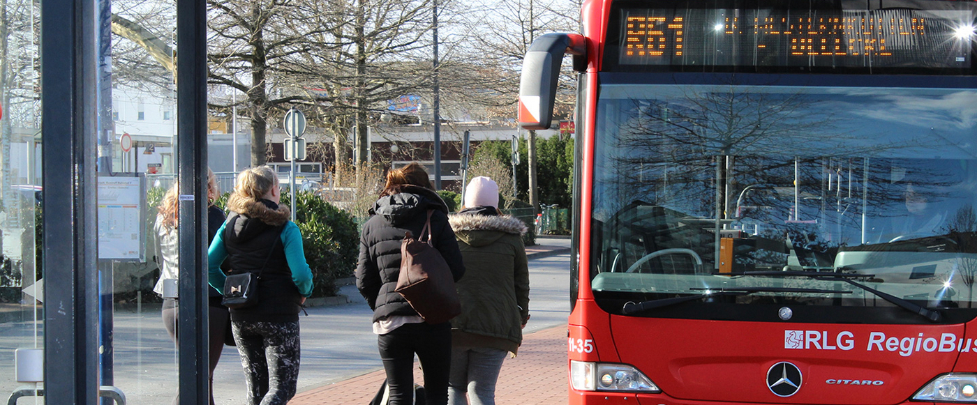 Bus hält an einer Haltestelle, mehrere Menschen laufen zum Bus.