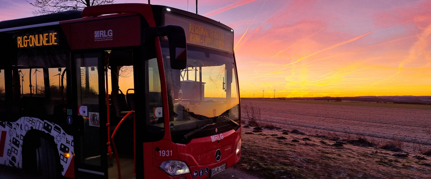 Front RegioBus links im Bild. Dämmerung. Rechts im Hintergrund stehen Windräder.