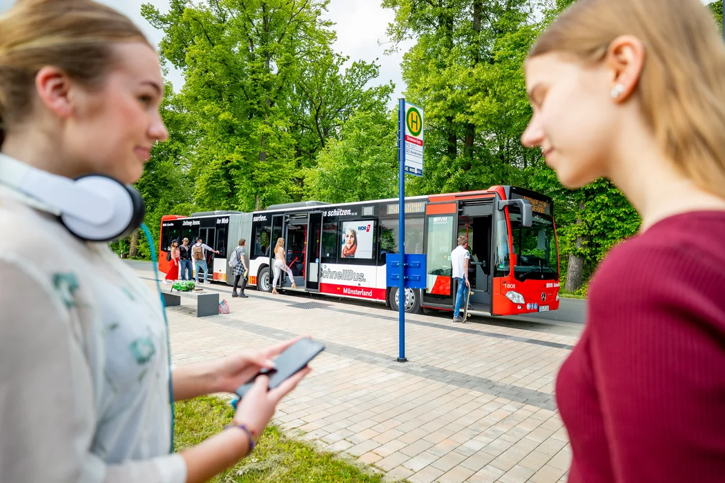Zwei Frauen steht im Vordergrund vor einem roten RLG Bus